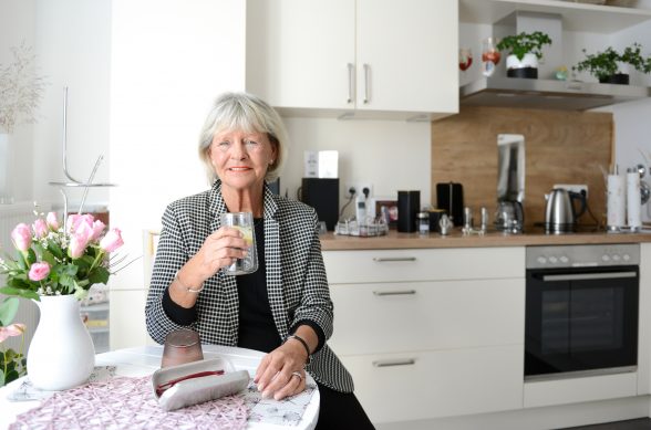 Eine ältere Frau sitzt am Küchentisch und hält ein Glas