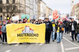 Mehrere Menschen laufen in einer Demonstration auf einer Straße und halten gemeinsam das Plakat der Mietendemo in den Händen